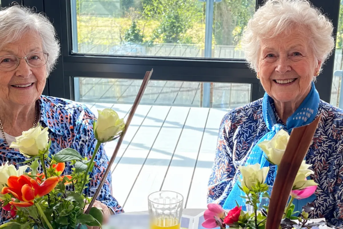 Two residents smiling at a table with a vase of roses and tulips
